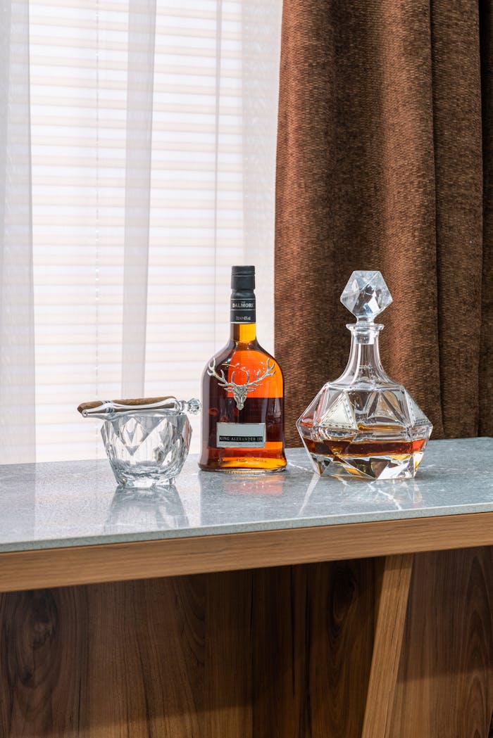 our-story Transparent bottle and decanter with expensive alcoholic drink near glass with cigar on table in house