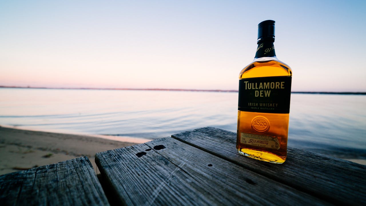 mobile-02 Tullamore Dew bottle on a wooden surface with serene beach background at sunset.